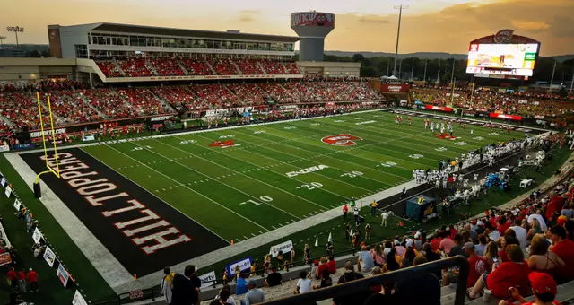 A packed football stadium at sunset, filled with excited fans in red, capturing the spirit of live sports and community.