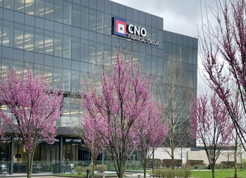 Modern glass office building with blooming pink trees and green grass under an overcast sky, evoking tranquility and renewal.