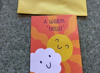 Colorful greeting card with "A WARM Hello" and bright sun; paired with a yellow envelope, evoking joy and friendliness.