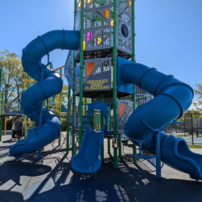 Colorful playground with twisting blue slides, tall towers, and sunny skies evokes joy and playful exploration.