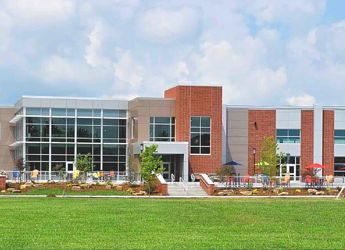 Modern community center with glass windows, colorful chairs, and a lawn, exuding a welcoming and tranquil atmosphere.