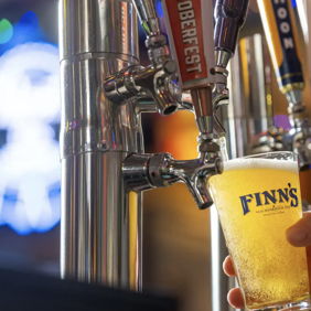 A hand pours golden, bubbly beer into a glass, evoking joy, relaxation, and community in a lively bar setting.