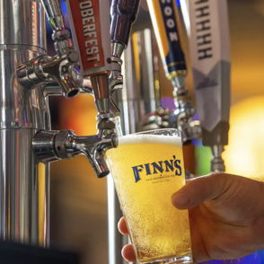 A hand pours golden, bubbly beer into a glass, evoking joy, relaxation, and community in a lively bar setting.