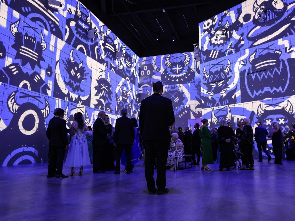 Vibrant art-filled space with blue and white abstract designs; elegant guests interact, creating a joyful, celebratory atmosphere.