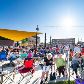 A vibrant outdoor crowd gathers in colorful chairs under sunny skies, evoking joy, community, and a cheerful atmosphere.