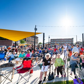 A vibrant outdoor crowd gathers in colorful chairs under sunny skies, evoking joy, community, and a cheerful atmosphere.