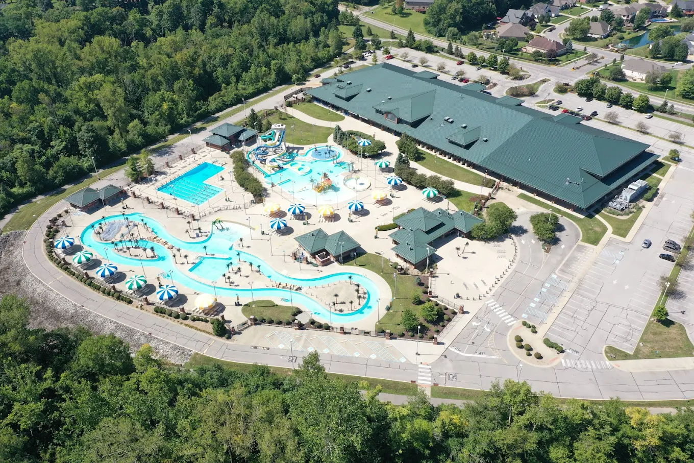 Aerial view of a vibrant water park with pools, slides, lounging areas, and greenery, evoking summer fun and relaxation.