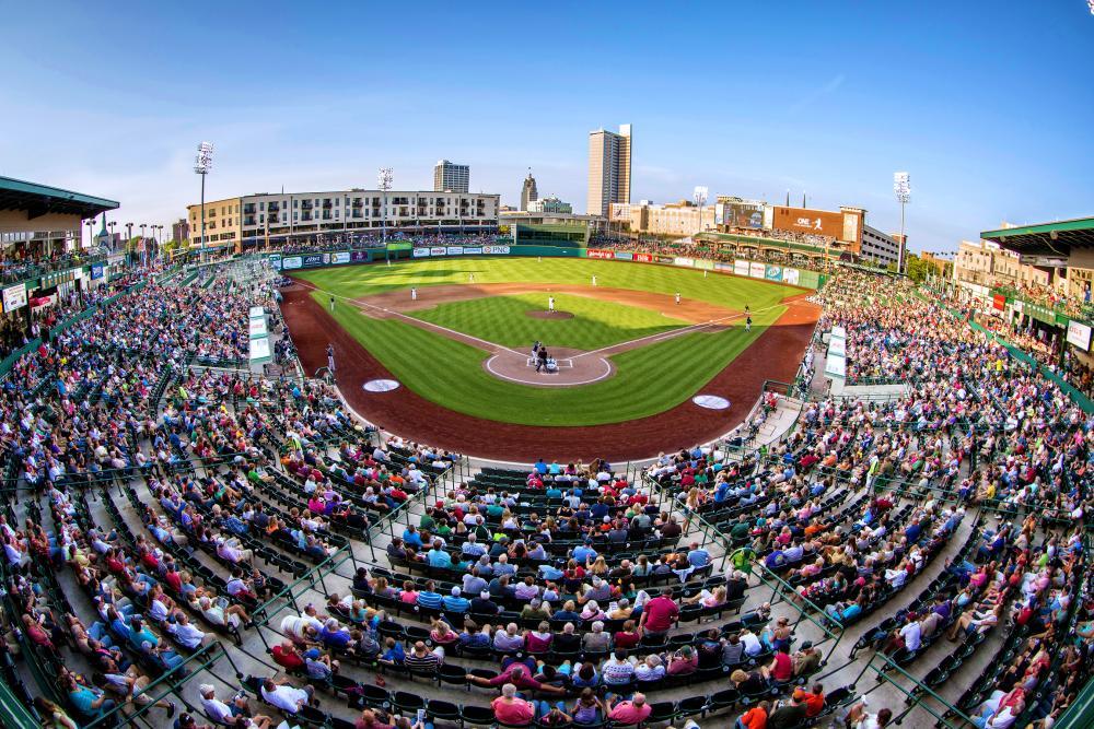 A lively baseball stadium filled with excited spectators under a clear blue sky, highlighting enjoyment and community spirit.