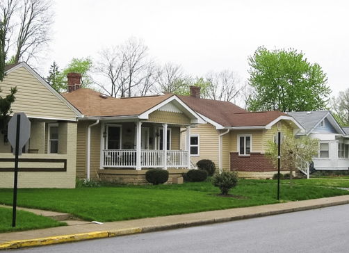A tranquil residential street with colorful houses, lush lawns, and trees evokes nostalgia and comfort in a serene setting.