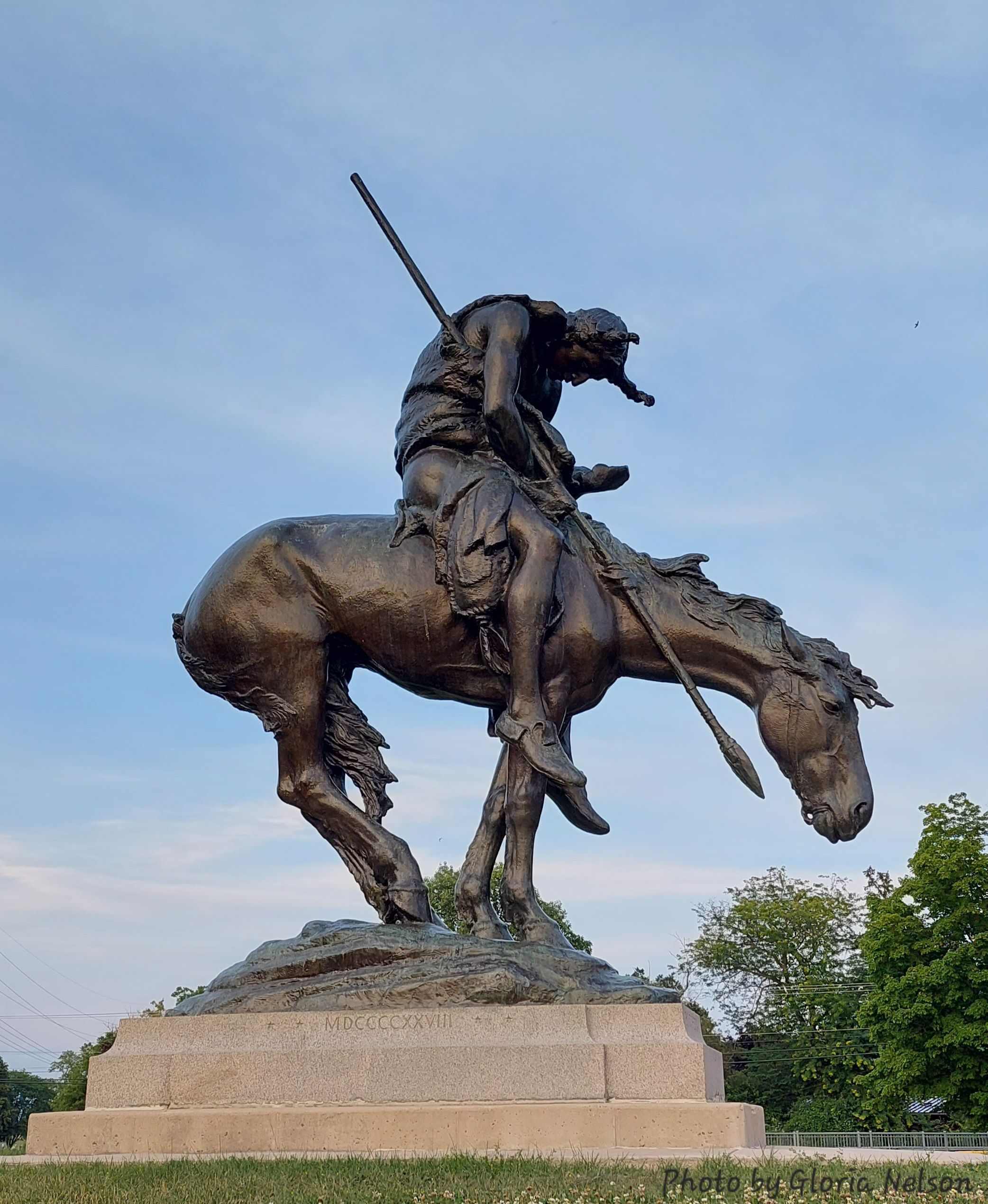 Bronze statue of a poised warrior on a dynamic horse, embodying strength and bravery against a tranquil sky backdrop.