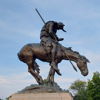 Bronze statue of a poised warrior on a dynamic horse, embodying strength and bravery against a tranquil sky backdrop.