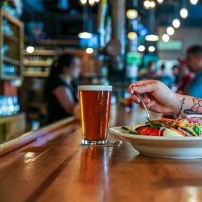 A cozy bar setting with a salad, drinks, and a tattooed diner, capturing a vibrant, relaxed atmosphere of friendship.