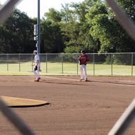 Baseball field scene through a chain-link fence, with players in uniform, evoking excitement, camaraderie, and nostalgia.