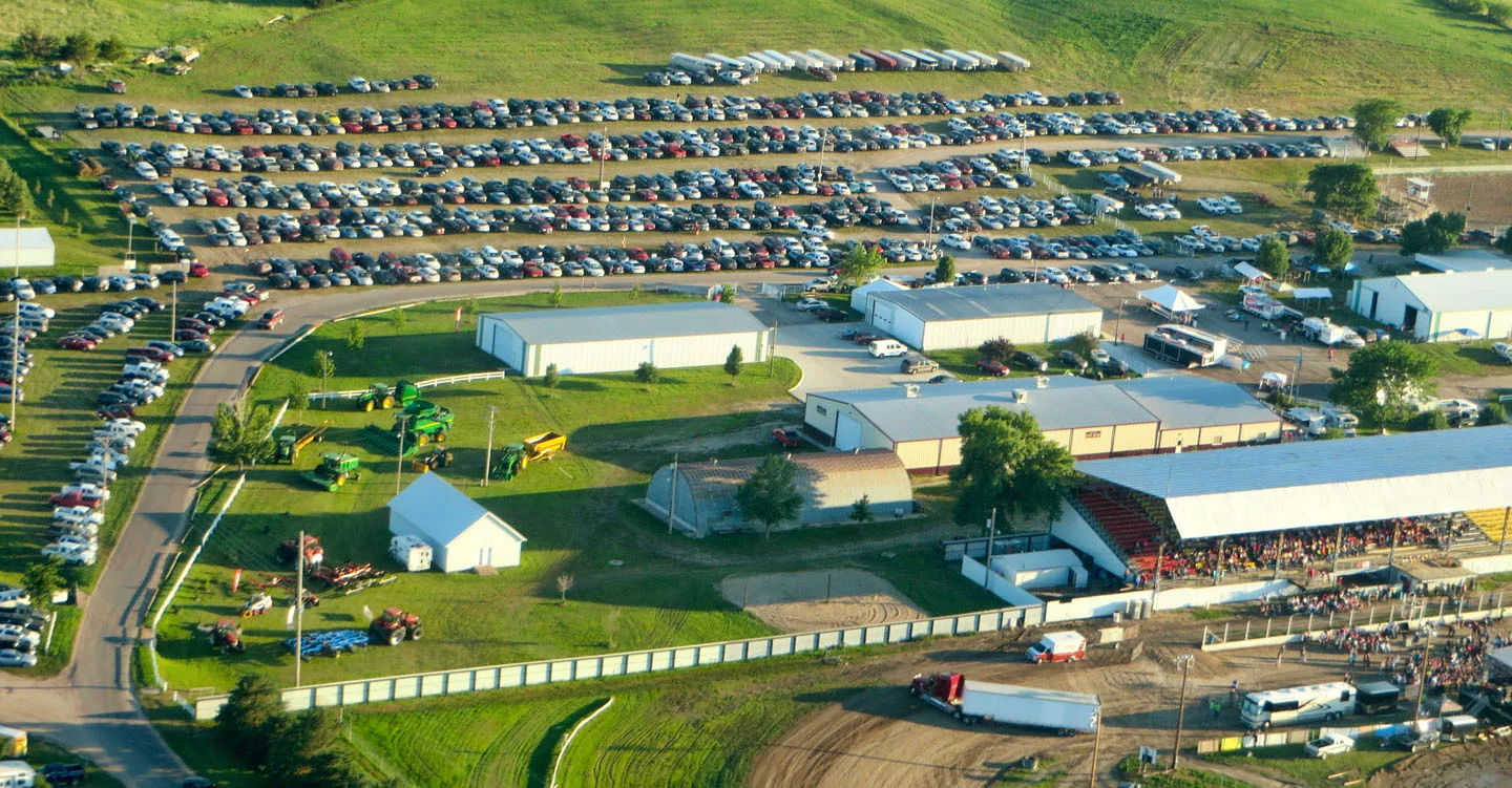 Aerial view of a lively fair with numerous cars, buildings, and green fields, evoking joy, nostalgia, and community spirit.
