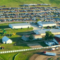 Aerial view of a lively fair with numerous cars, buildings, and green fields, evoking joy, nostalgia, and community spirit.
