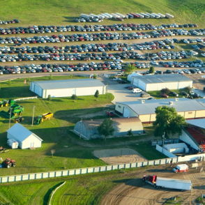 Aerial view of a lively fair with numerous cars, buildings, and green fields, evoking joy, nostalgia, and community spirit.