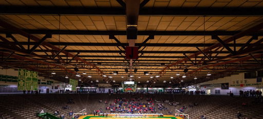 A vibrant indoor sports arena with a basketball court, featuring colorful markings and a mix of excited fans and empty seats.