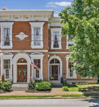 Charming two-story brick house with elegant windows, surrounded by greenery, evokes warmth, nostalgia, and a sense of community.