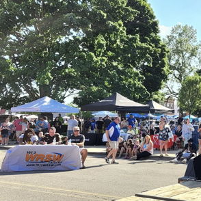 Vibrant outdoor festival scene with a female performer engaging a diverse crowd, colorful tents, and a lively atmosphere.