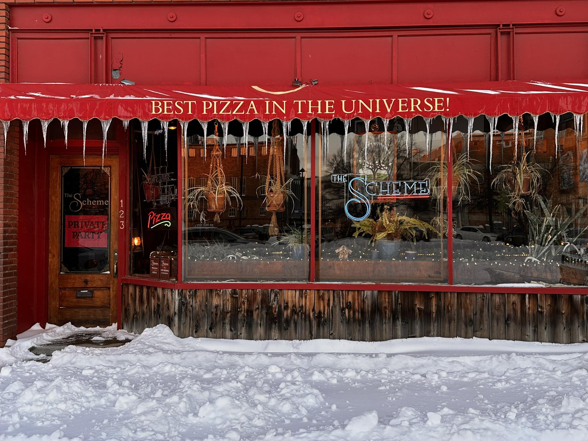 Cozy pizza restaurant with a red awning claims "BEST PIZZA IN THE UNIVERSE!" Icicles and snow create a chilly winter scene.