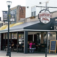 Cozy restaurant "Dawson's on Main" features a welcoming exterior and lively diners, evoking warmth and community connection.