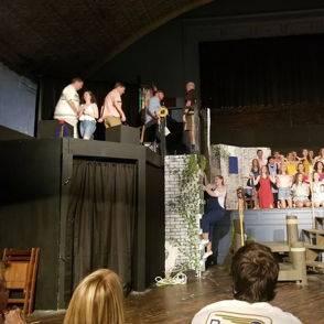 The image shows a lively theater performance with a large cast in dynamic poses, enhancing themes of excitement and collaboration.