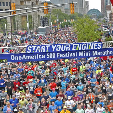 A lively marathon starting line with excited runners and a "START YOUR ENGINES" banner, showcasing a vibrant, festive atmosphere.
