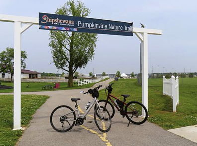 Scenic pathway to Pumpkinvine Nature Trail with bicycles parked, showcasing a peaceful, lush outdoor environment.