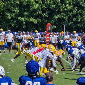 Football practice scene with players in yellow and blue uniforms, focused on their play under a sunny, vibrant atmosphere.
