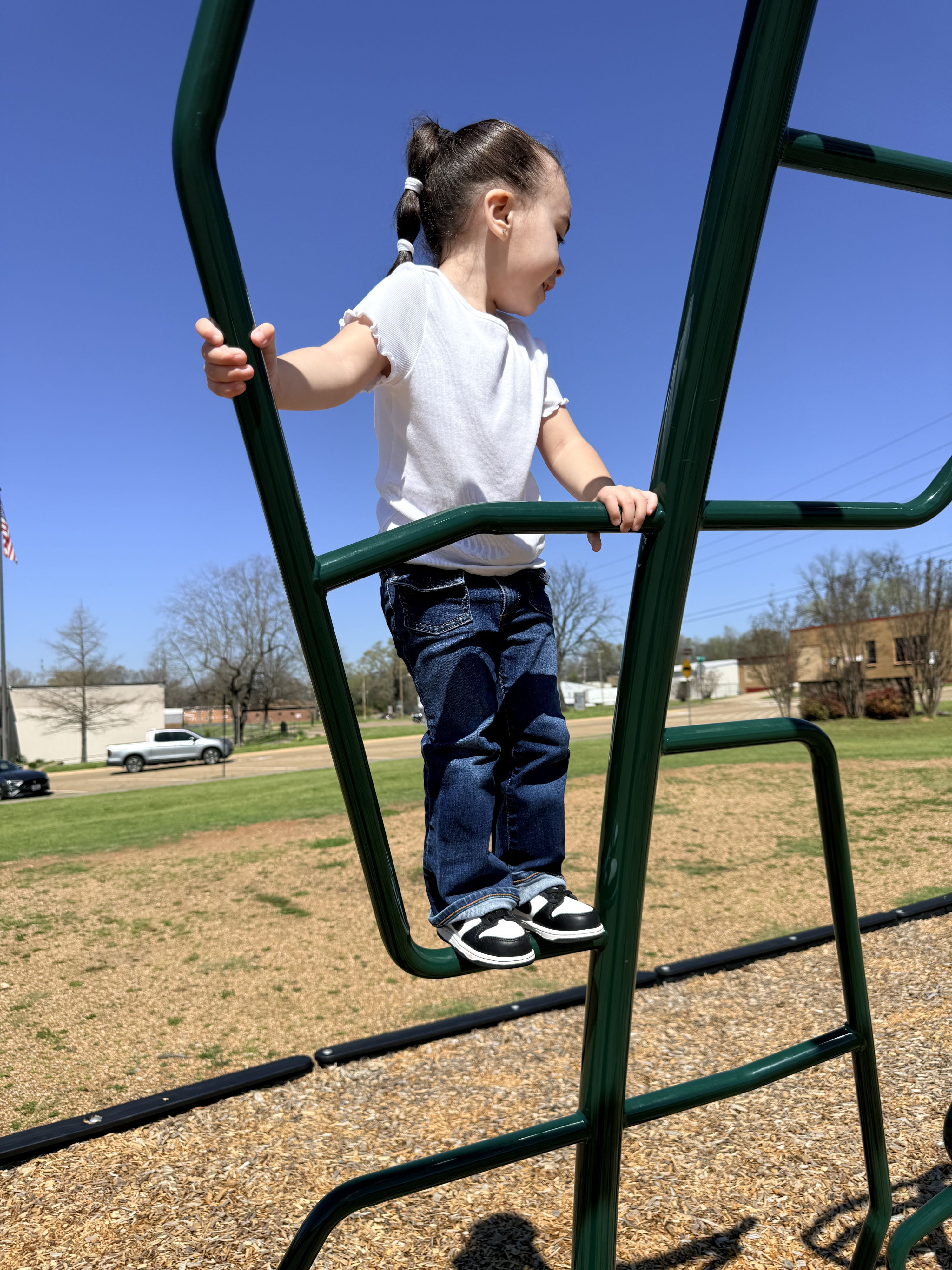A child in a white shirt and jeans climbs a playground, embodying joy, curiosity, and the spirit of carefree play.