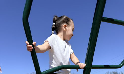 A child in a white shirt and jeans climbs a playground, embodying joy, curiosity, and the spirit of carefree play.