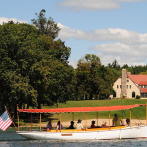 Lakeside scene with a boat and people, a red-roofed building, lush greenery, and a clear sky, evoking tranquility and leisure.