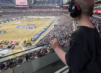 A young boy in headphones shares excitement in a lively indoor stadium during a vibrant motorsport event.