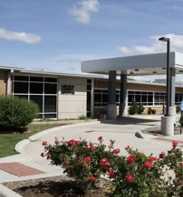 Modern building with clean lines, welcoming entrance, surrounded by colorful blooms and neat landscaping, evoking calm positivity.