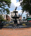 Charming public square with an ornate fountain, surrounded by trees and flowers, evoking tranquility in a bustling town.