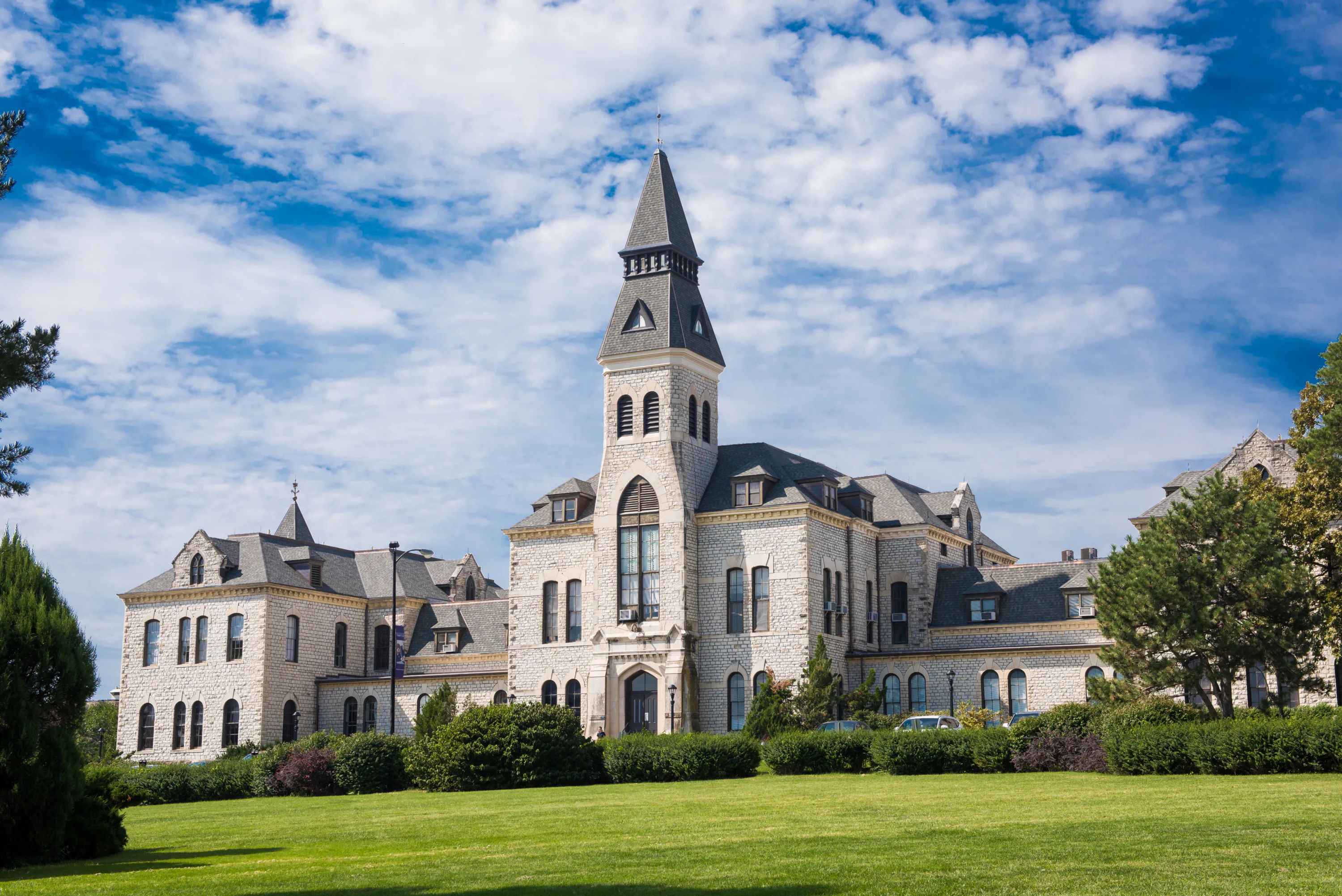 Historic building with a tall tower, mixed architecture, surrounded by lush greenery and a bright sky, evoking nostalgia and serenity.