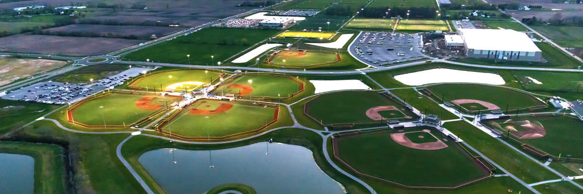 Aerial view of a sports complex with illuminated baseball fields, open spaces, and a serene atmosphere, evoking community and nostalgia.