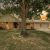 Charming brick house with a lush lawn, large tree, and a colorful sunset, evoking comfort and tranquility.
