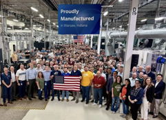 Group of smiling people in a manufacturing facility, proudly holding a flag, capturing community spirit and teamwork.