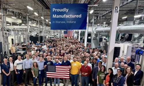 Group of smiling people in a manufacturing facility, proudly holding a flag, capturing community spirit and teamwork.