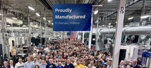 Group of smiling people in a manufacturing facility, proudly holding a flag, capturing community spirit and teamwork.