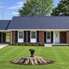 Charming one-story home with a sloped roof, brick, white columns, and a lush lawn, evoking warmth and nostalgia.