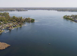 Aerial view of a serene lake surrounded by greenery and homes, reflecting nature's beauty and evoking calm and nostalgia.