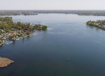 Aerial view of a serene lake surrounded by greenery and homes, reflecting nature's beauty and evoking calm and nostalgia.
