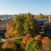 Aerial view of a campus with vibrant autumn foliage, a brick building, and a tranquil atmosphere under a bright blue sky.