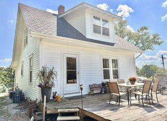 Charming white house with a porch, patio furniture, surrounded by greenery and a blue sky, evoking warmth and tranquility.