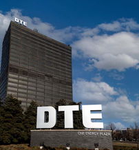 Modern skyscraper with "DTE" signage, sleek facade, blue sky, and greenery, evoking innovation and stability.