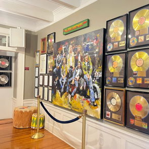 Wall displaying framed gold and platinum music awards, colorful painting, evoking celebration, achievement, and artistic respect.