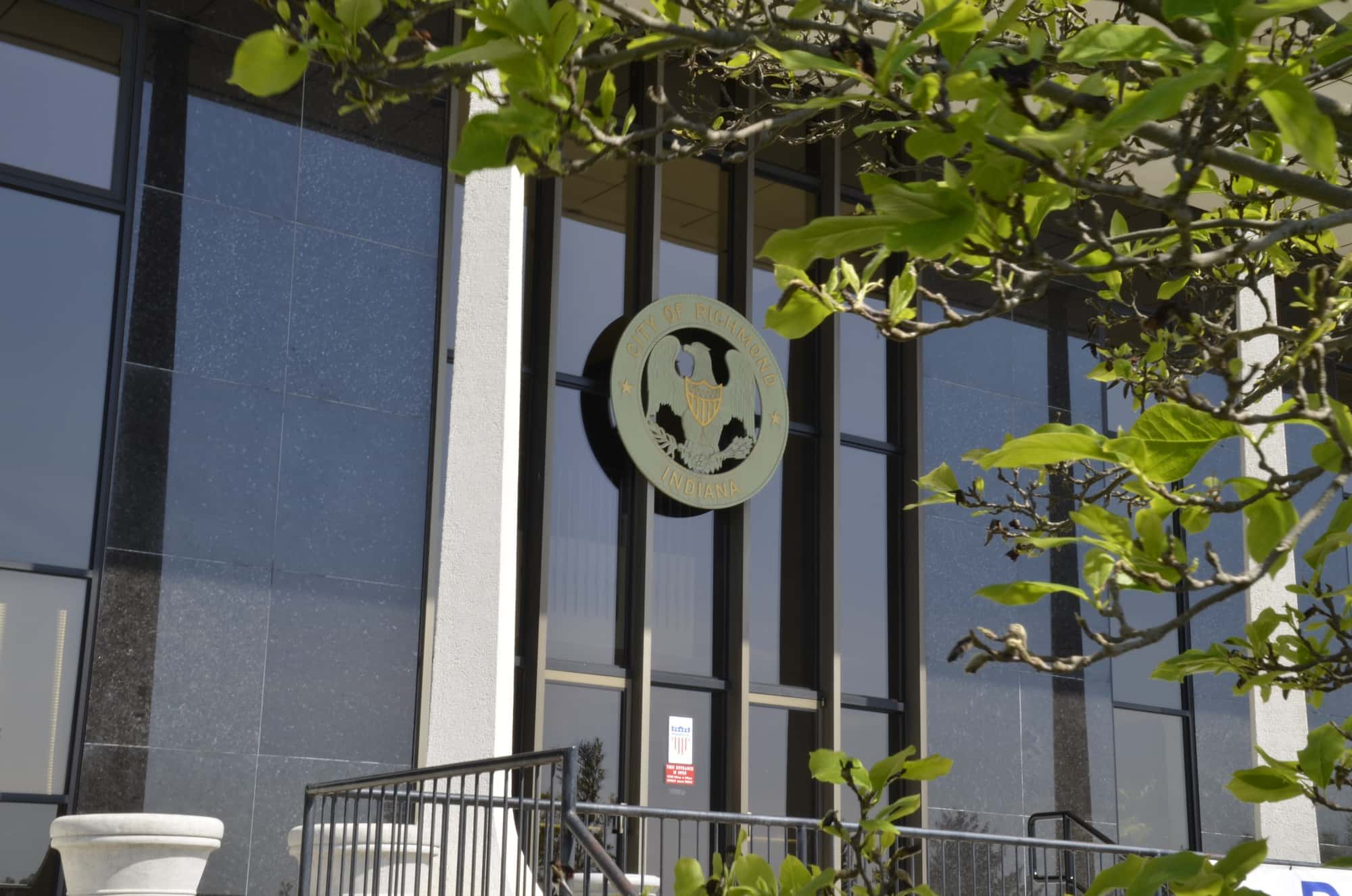 Modern building with glass windows, central emblem, greenery, conveying trust, stability, and a welcoming atmosphere.