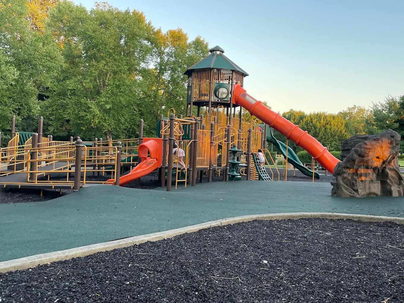 Brightly colored playground with a large slide, climbing areas, surrounded by trees, evokes joy and adventure for children.
